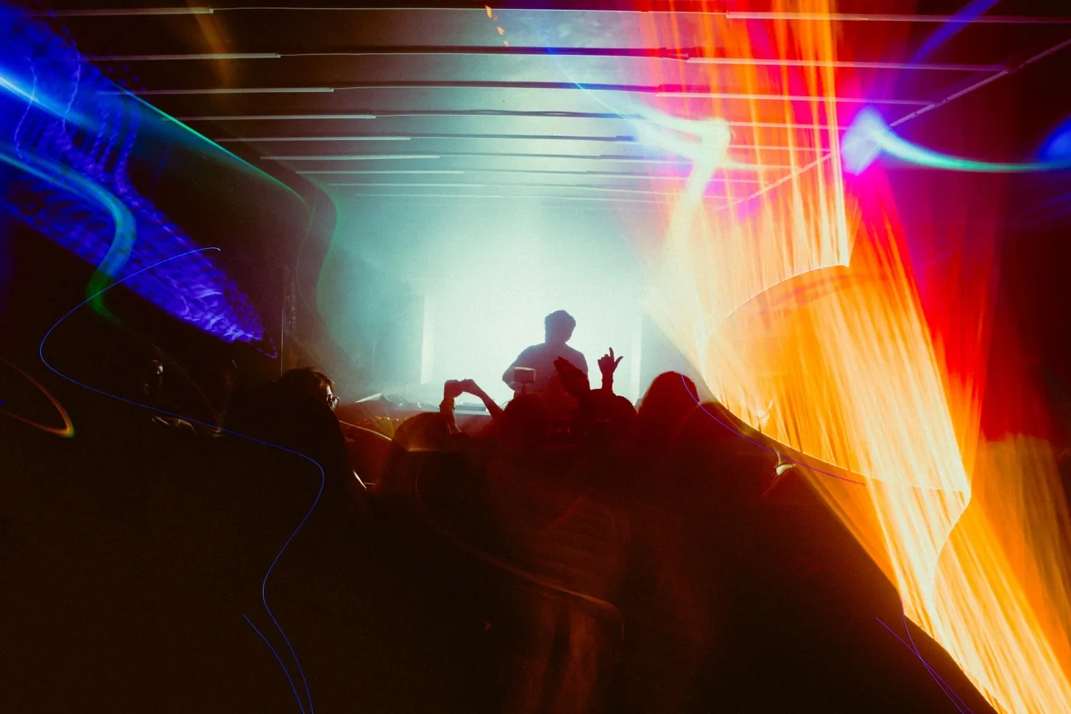 Crowd silhouettes beneath vivid blue and orange light trails at Project Kulture