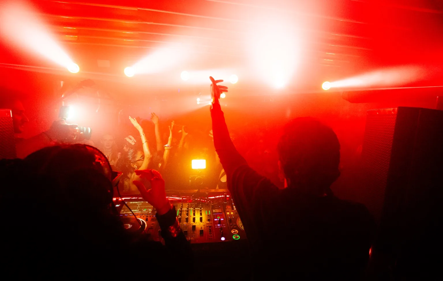 Raised hands at the DJ booth under red stage lights at Project Kulture.
