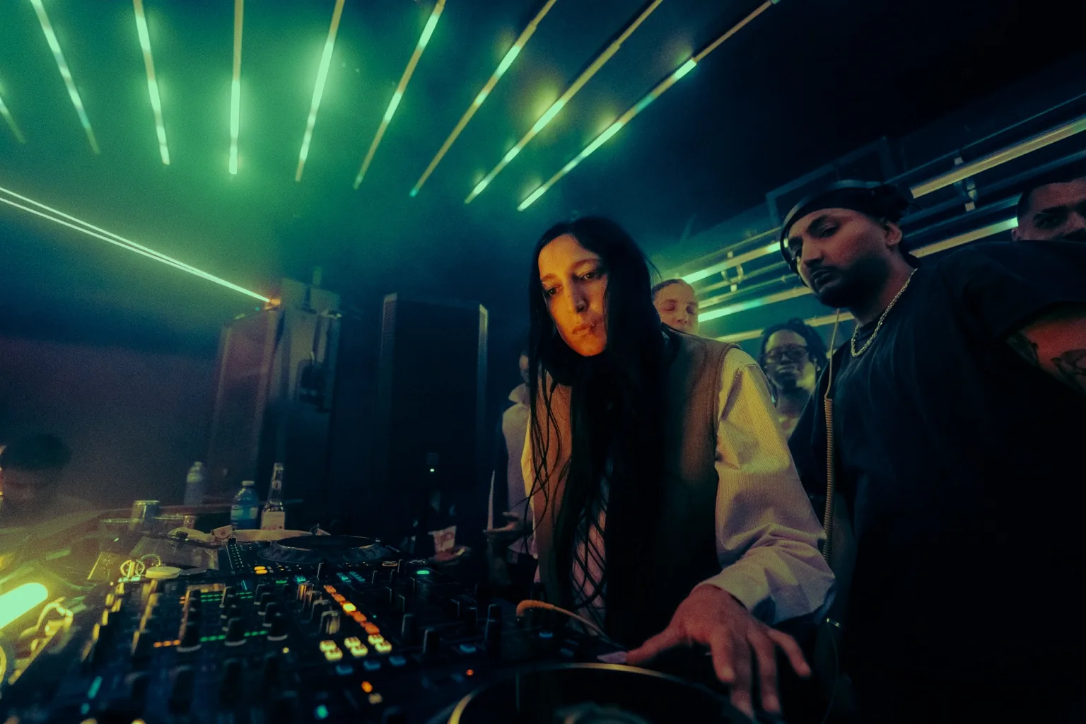 Two DJs at the mixer beneath green beams at Project Kulture.